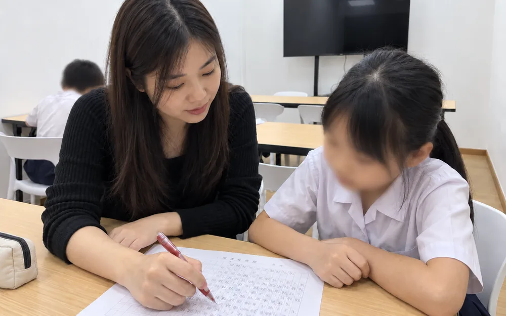 Primary Chinese lesson at WhaleYou Learning with the teacher checking a student's work